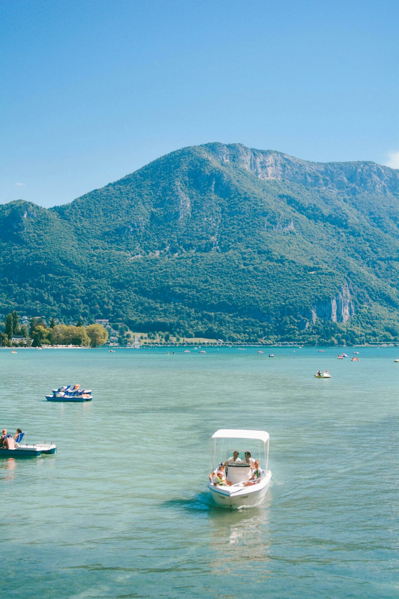Leisure boats on Lake Annecy, France against a mountain backdrop on a sunny day.